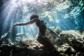   Freediver Model Natalia embracing sunlight beaming through waters surface cenote Dos Ojos Mexico  